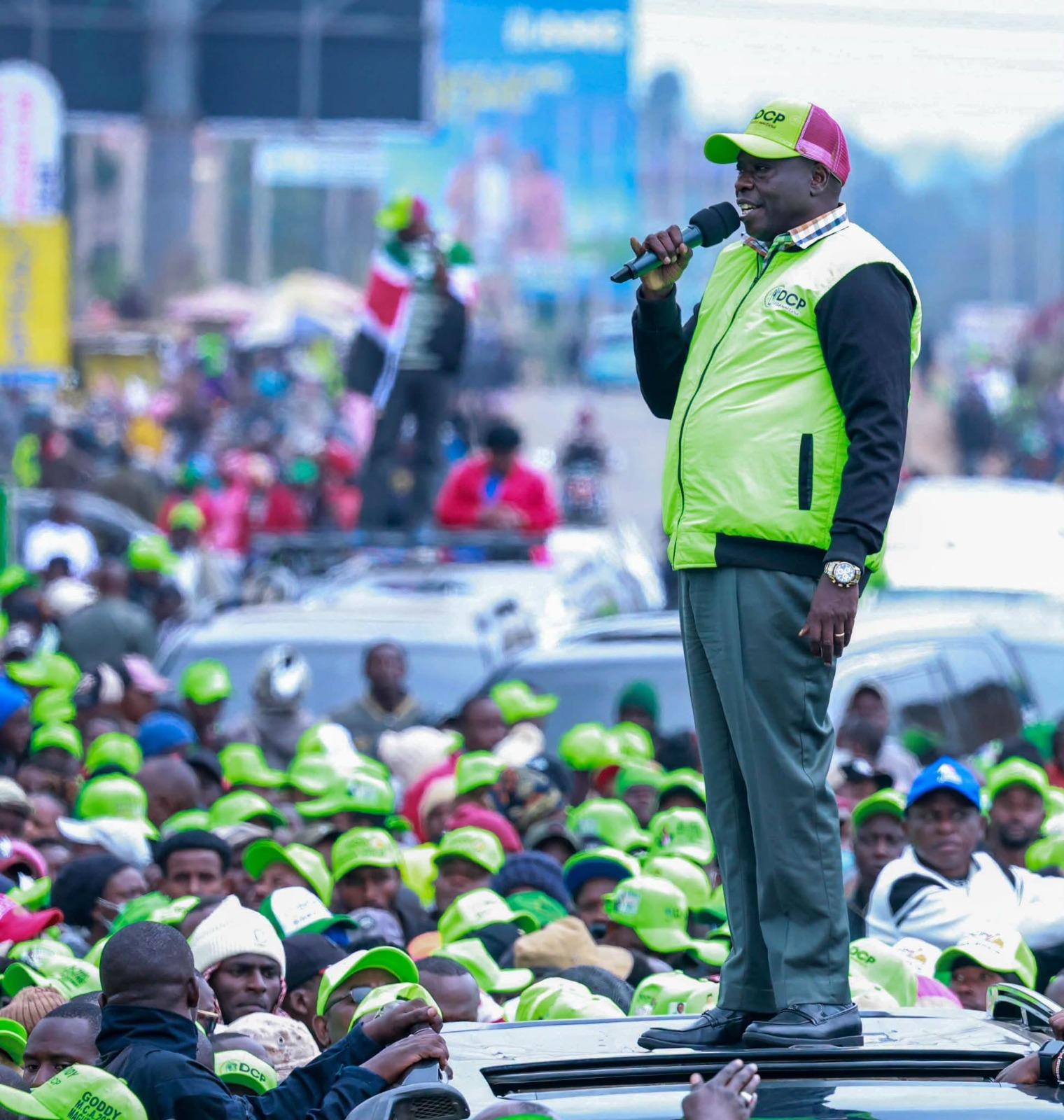 Rigathi Gachagua in a DCP cap and vest, speaking to a crowd from a car roof